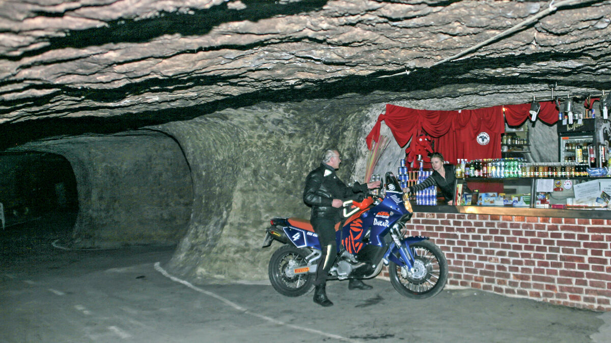 Stollen im Fels mit einer Bar aus Backstein, davor ein Mann neben einer blau-orangen KTM
